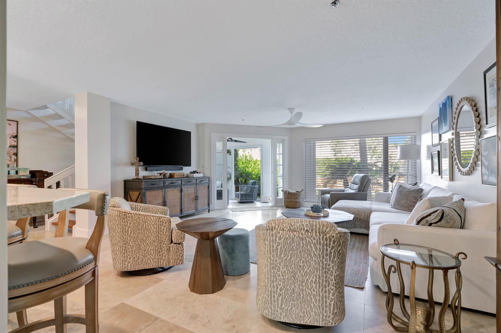 A bright living room features a white sofa, patterned armchairs, a television, and glass doors — 1000 N Us Highway 1 # 658, Jupiter FL 33477, JUPITER, FL