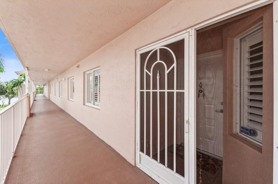 An outdoor apartment walkway with a white security screen door and a window with shutters — 5874 Crystal Shores Drive # 304, Boynton Beach FL 33437, BOYNTON BEACH, FL