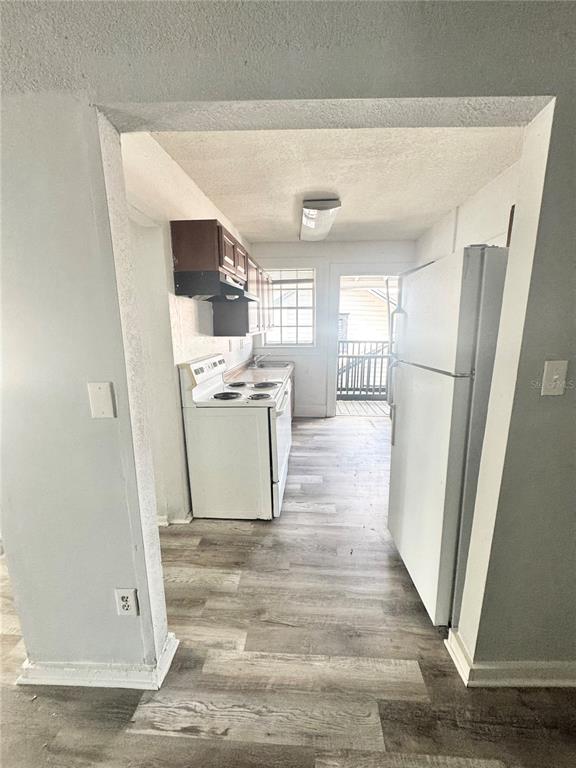 A kitchen features white appliances, wood-look flooring, and a doorway leading to an outdoor balcony — 704 CORDOVA DRIVE UNIT 7, ORLANDO, FL