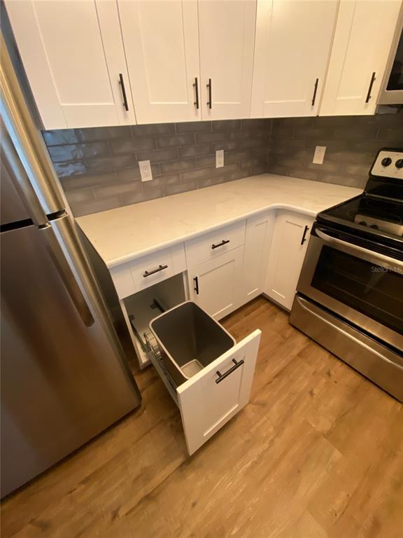 A kitchen features white cabinets, a pull-out trash bin, stainless steel appliances, and gray backsplash — 823 CAMARGO WAY UNIT 105, ALTAMONTE SPRINGS, FL
