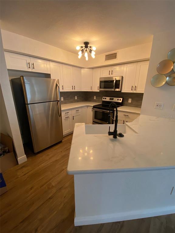A kitchen features white cabinets, stainless steel appliances, a marble-look countertop, and wood-style flooring — 823 CAMARGO WAY UNIT 105, ALTAMONTE SPRINGS, FL
