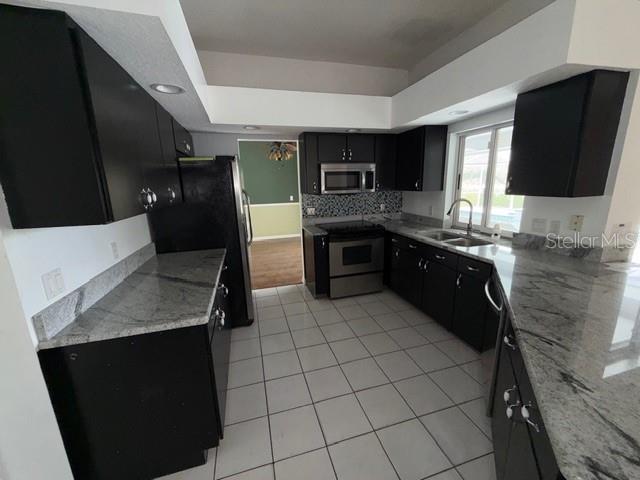 A kitchen with dark cabinets, granite countertops, stainless steel appliances, and white tile flooring — 1235 ODONIEL LOOP S, LAKELAND, FL