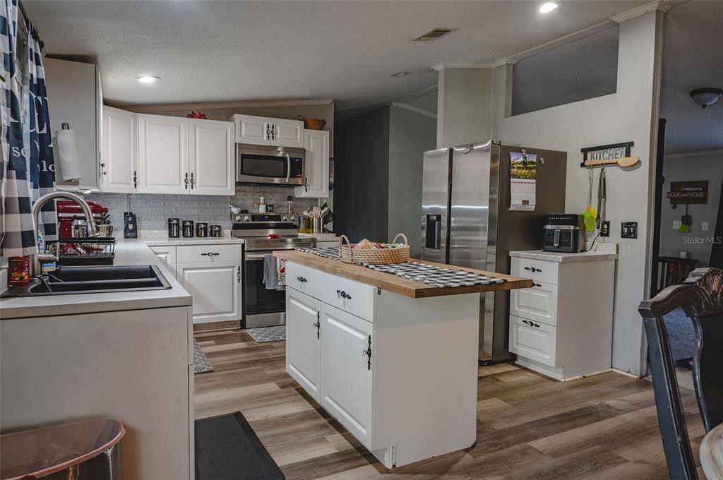 A kitchen features white cabinetry, stainless steel appliances, a wood-topped island, and wood-look flooring — 7296 NW 170TH STREET, TRENTON, FL