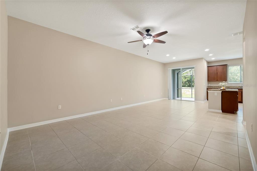 An open-concept living area with beige tile flooring, neutral walls, and an adjacent kitchen — 342 REED GRASS DRIVE, OVIEDO, FL