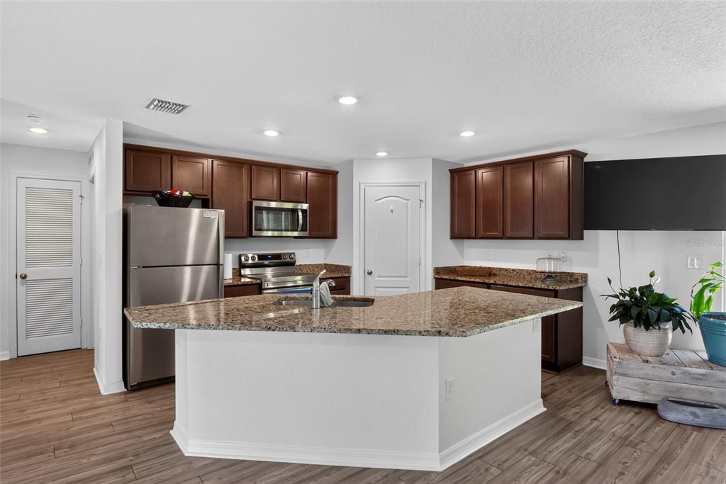 A kitchen with dark wood cabinets, granite countertops, stainless steel appliances, and wood-look flooring — 39 SEDERHOLM PATH, PALM COAST, FL