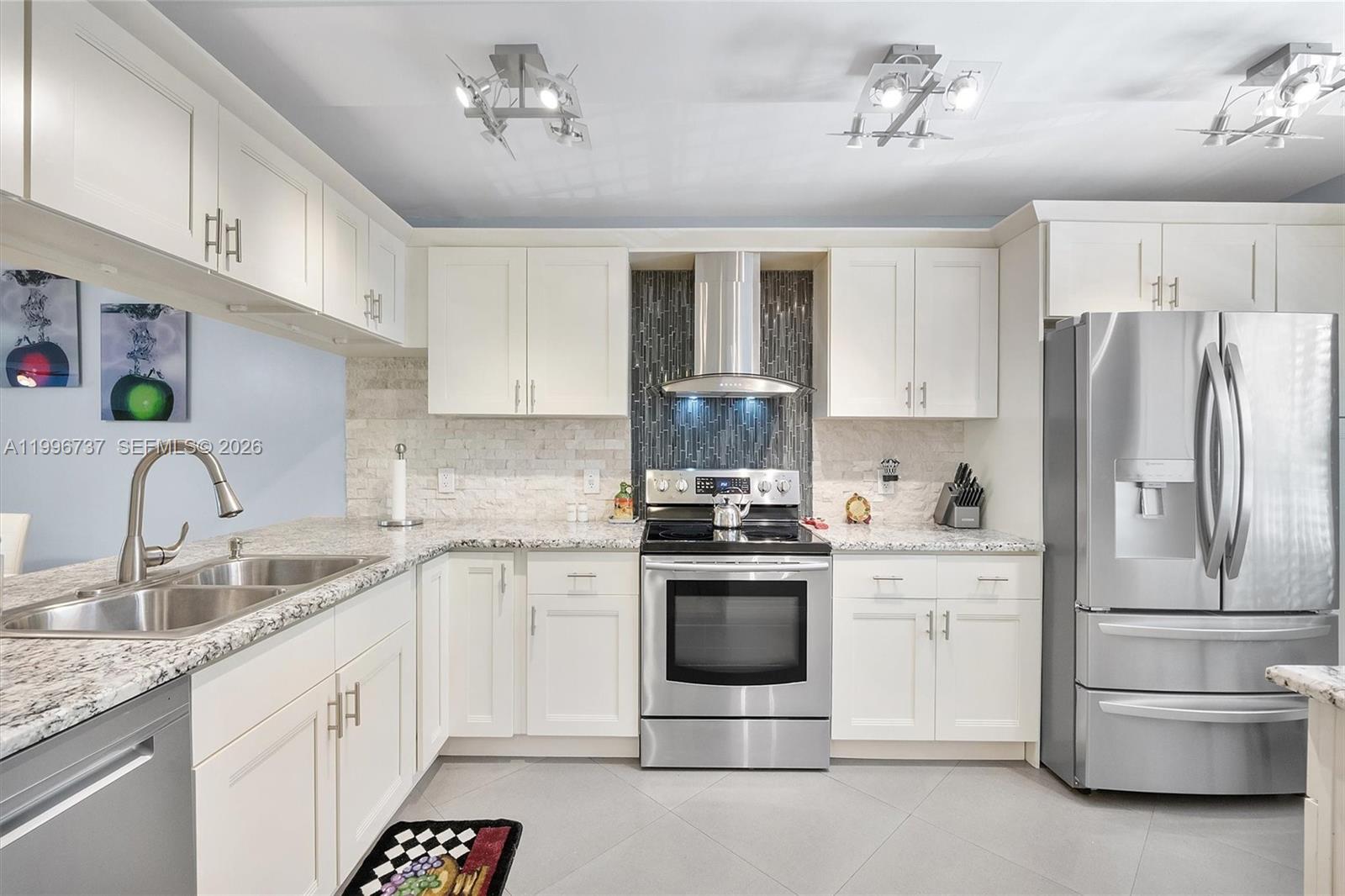 A kitchen features white cabinets, granite countertops, stainless steel appliances, and a tiled backsplash — 3503 Oaks Way # 308, Pompano Beach FL 33069, POMPANO BEACH, FL