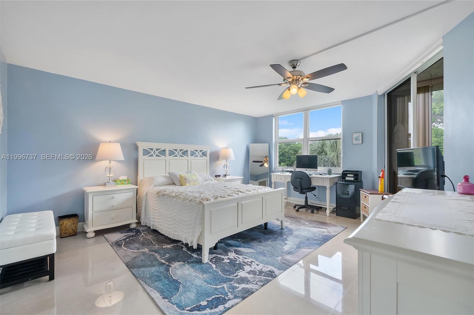 A bedroom features a white bed, a desk area, and a blue patterned area rug — 3503 Oaks Way # 308, Pompano Beach FL 33069, POMPANO BEACH, FL
