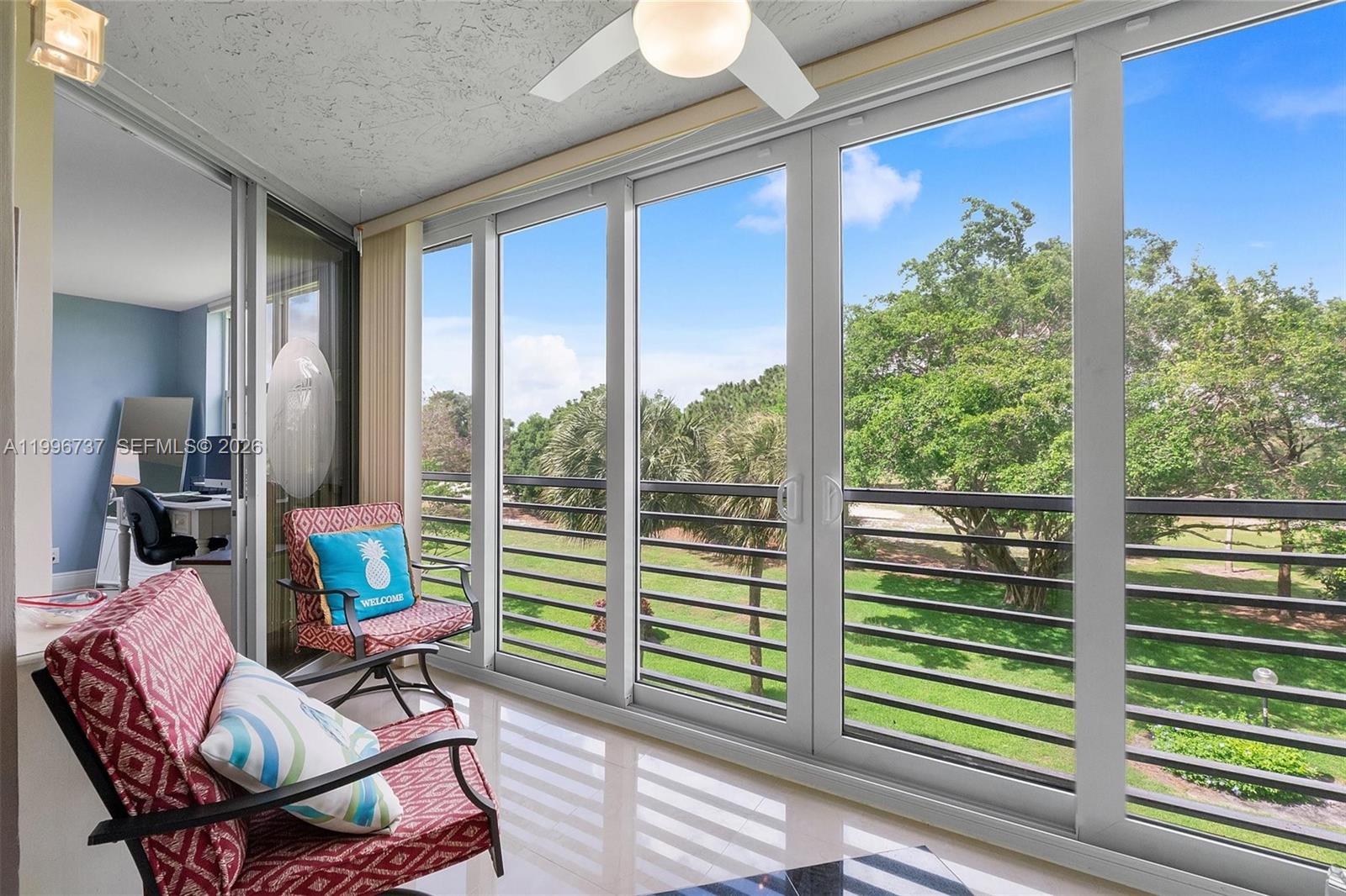 A sunroom features red patterned chairs, tile flooring, and large sliding glass doors overlooking trees — 3503 Oaks Way # 308, Pompano Beach FL 33069, POMPANO BEACH, FL