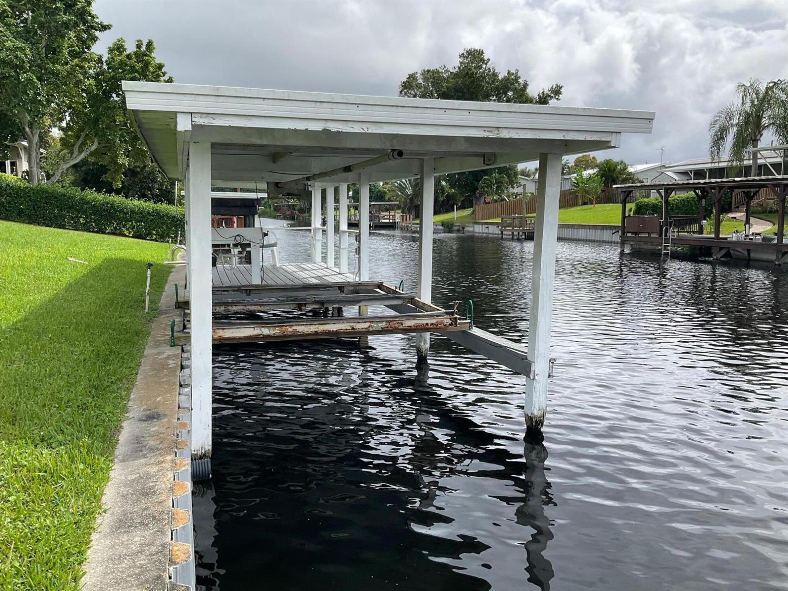 A boat lift with a white roof sits over a canal next to a grassy lawn — 2518 SE 32nd Street, Okeechobee FL 34974, OKEECHOBEE, FL