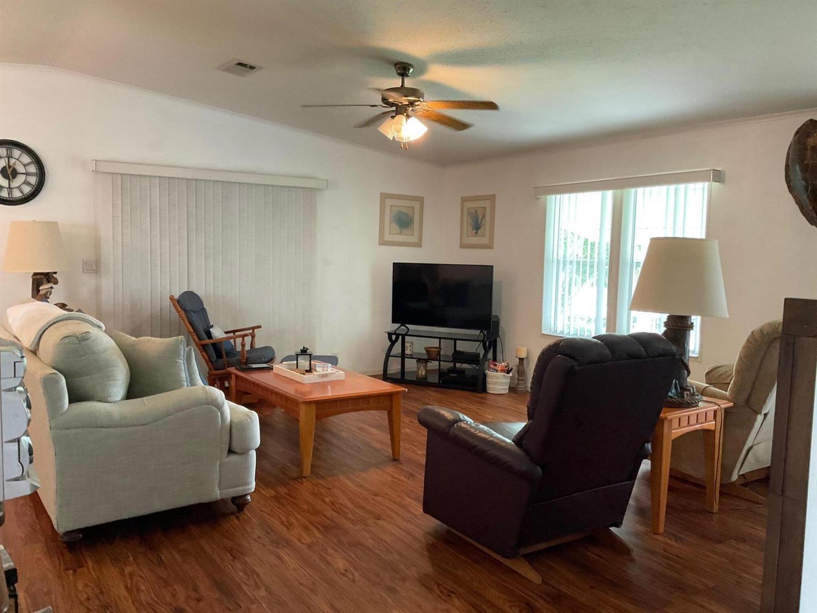 A living room features wood-look flooring, a ceiling fan, a television, and various seating options — 2518 SE 32nd Street, Okeechobee FL 34974, OKEECHOBEE, FL