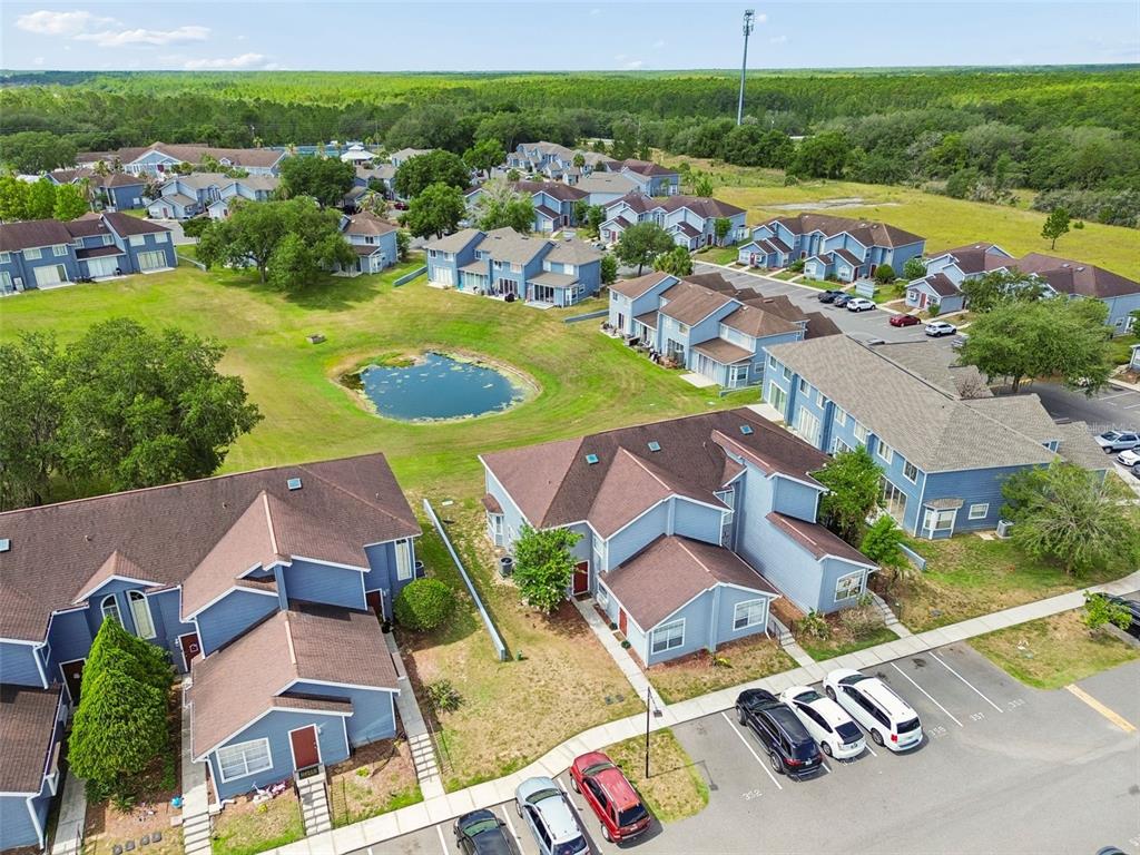 An aerial view shows blue multi-family residential buildings surrounding a small pond and parking area — 668 CARIBBEAN DRIVE, DAVENPORT, FL
