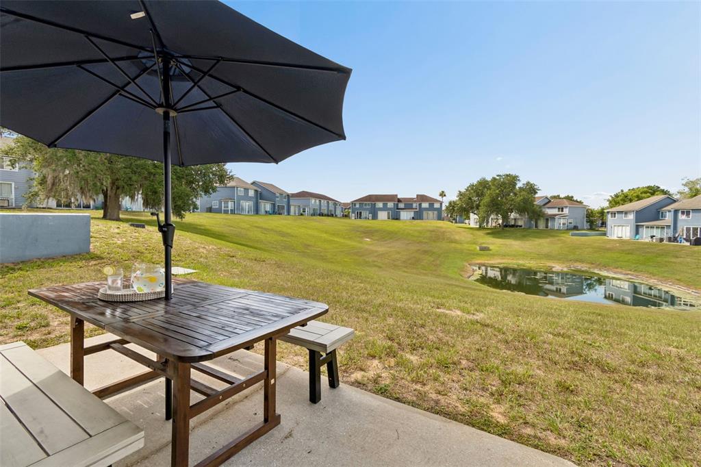 A patio with a wooden table and umbrella overlooks a grassy hill and a small pond — 668 CARIBBEAN DRIVE, DAVENPORT, FL