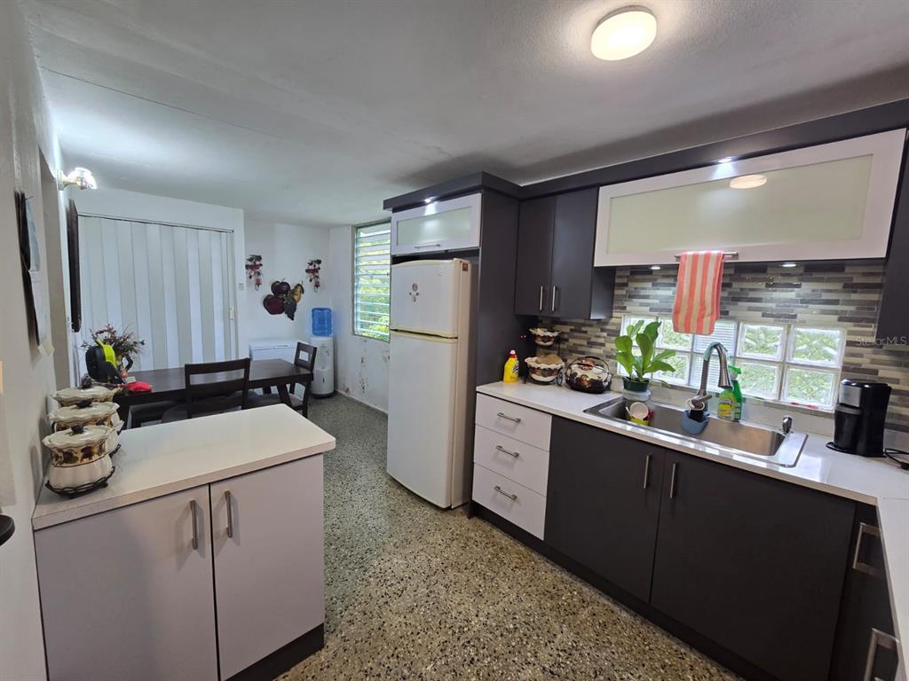 A kitchen with dark and white cabinetry, a white refrigerator, and a dining area nearby — SR 182 Km. 15.6 BO GUAYABOTAS, YABUCOA, PR