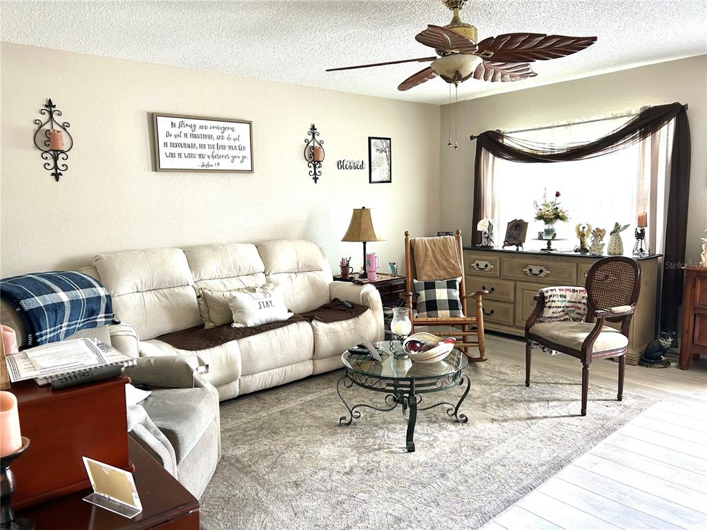 A living room features a beige sofa, a rocking chair, a coffee table, and a ceiling fan — 11909 BAYONET LANE UNIT 113A, NEW PORT RICHEY, FL