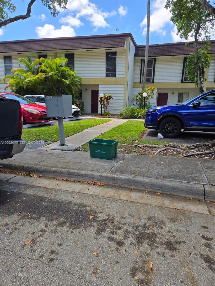 A two-story residential building exterior features a sidewalk, parked cars, and a green bin — HOLLYWOOD, FL