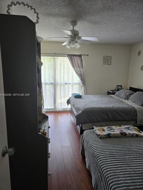 A bedroom features wood-look flooring, a ceiling fan, and two beds near a window — HOLLYWOOD, FL