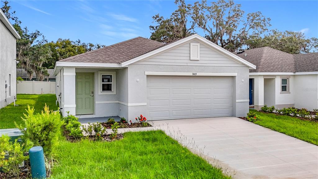 A single-story house with a light gray exterior, a two-car garage, and a green door — 31115 SILVER STAGE DRIVE, BROOKSVILLE, FL