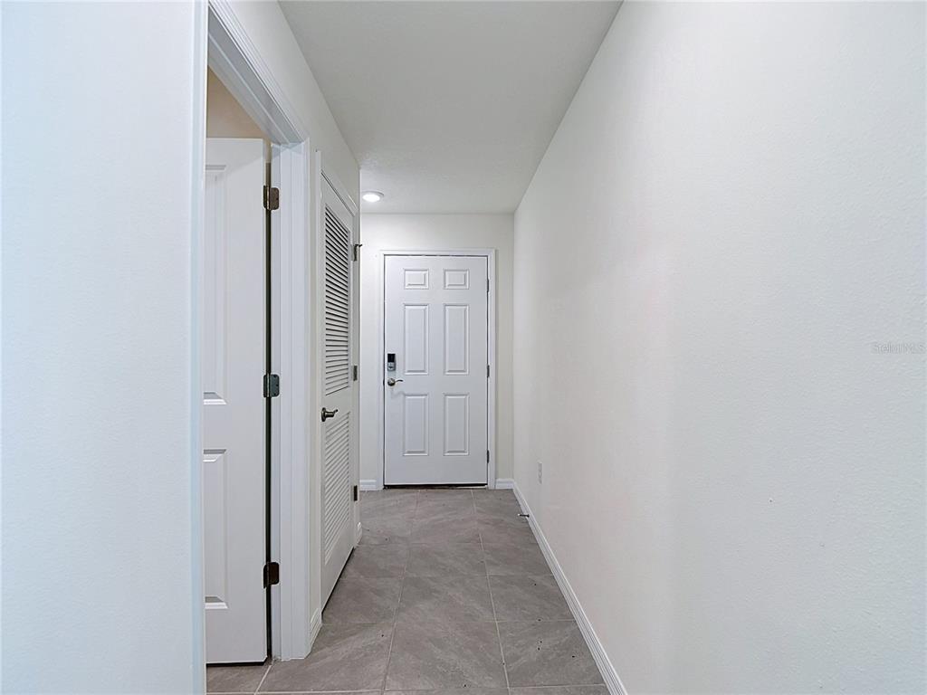 A hallway with white walls, gray tile flooring, and a white front door — 31115 SILVER STAGE DRIVE, BROOKSVILLE, FL