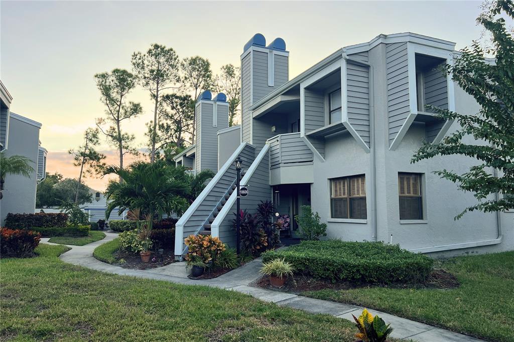 A two-story gray apartment building features an exterior staircase and a landscaped front yard — 10606 LONGWOOD DRIVE UNIT 203B, SEMINOLE, FL