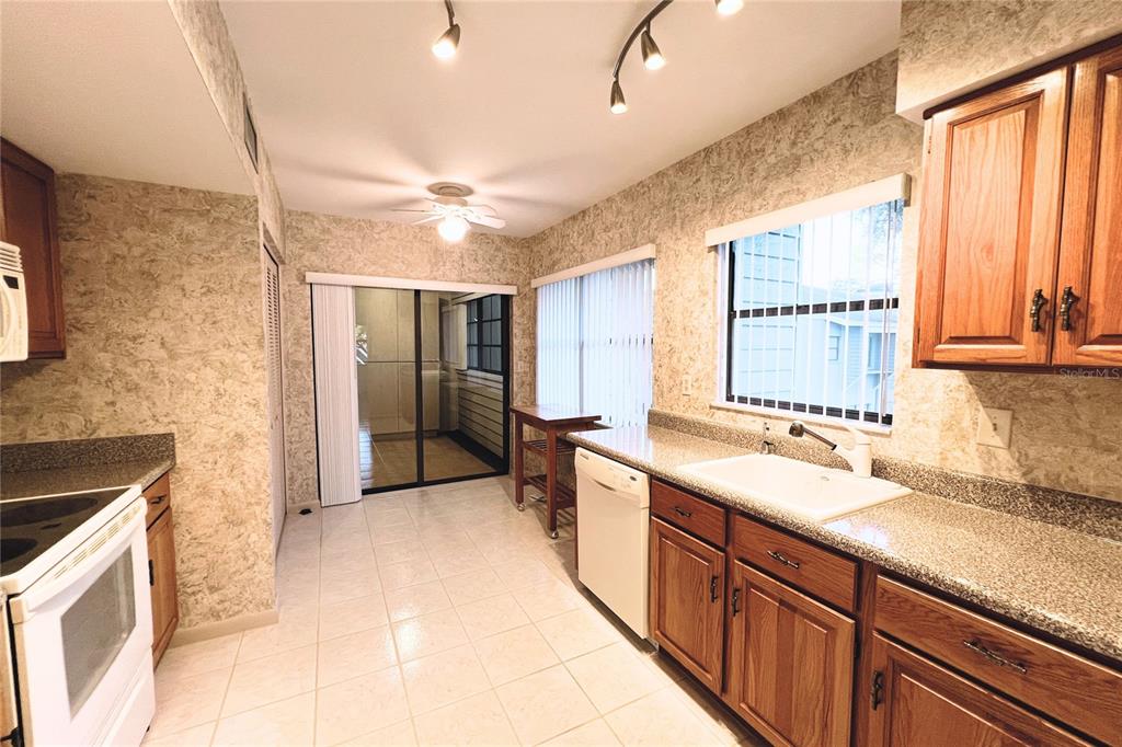 A kitchen with wood cabinets, granite countertops, tile flooring, and a sliding glass door — 10606 LONGWOOD DRIVE UNIT 203B, SEMINOLE, FL