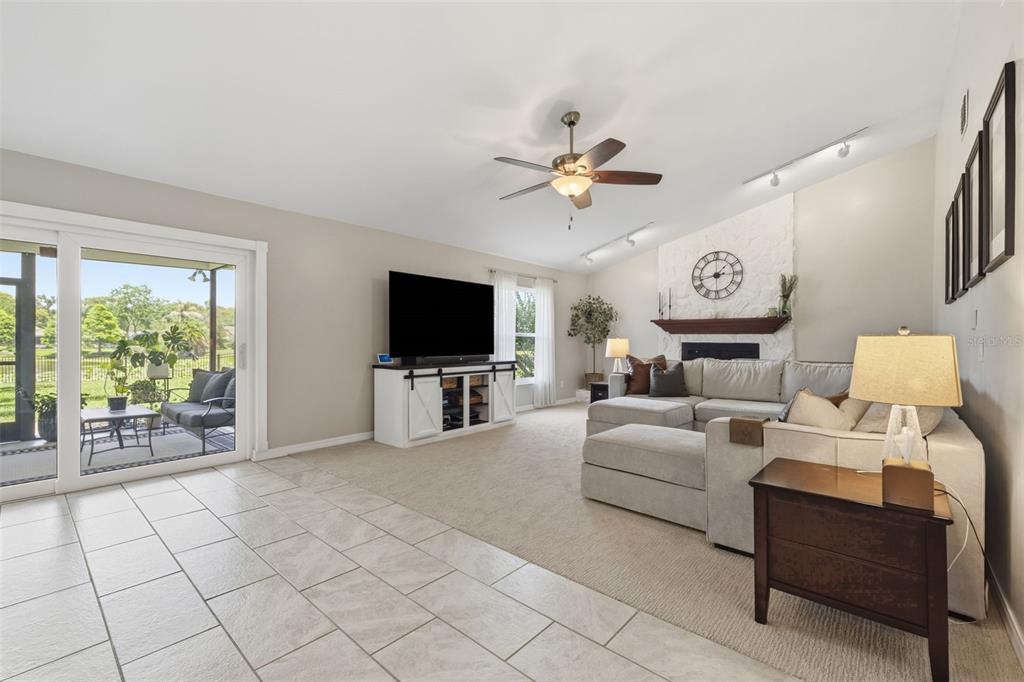A living room with a stone fireplace, sectional sofa, ceiling fan, and sliding glass doors — 17508 BRANDYWINE DRIVE, LUTZ, FL