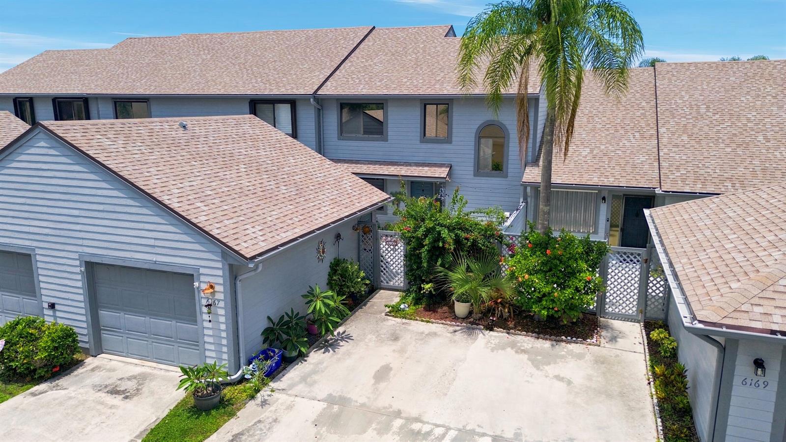 An exterior view of two adjacent townhomes with gray siding, shingled roofs, and concrete driveways — 6167 SE Georgetown Place, Hobe Sound FL 33455, HOBE SOUND, FL