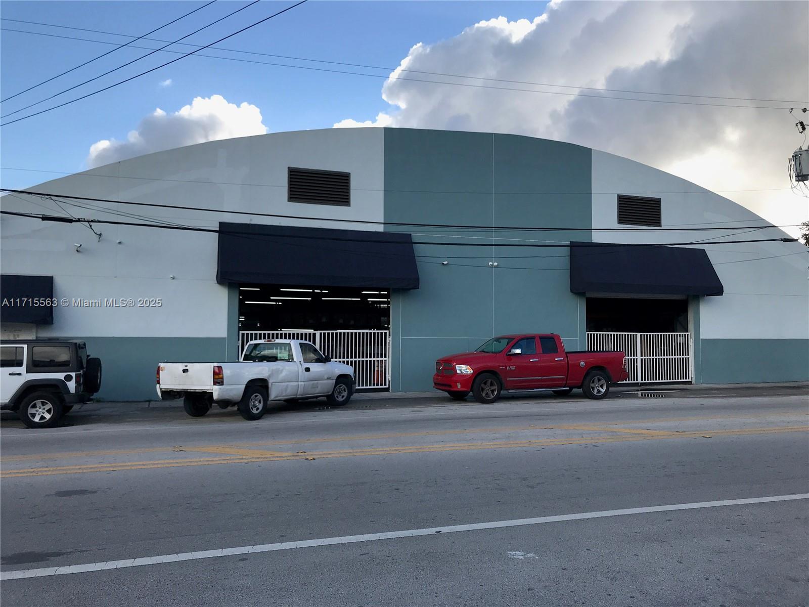 A commercial building with a curved roof features two garage bays and parked pickup trucks — 1628 NW 28th St, Miami FL 33142, MIAMI, FL