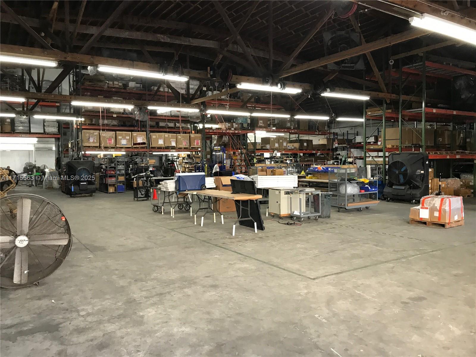 A large, open warehouse space features high ceilings, industrial lighting, storage racks, and concrete floors — 1628 NW 28th St, Miami FL 33142, MIAMI, FL