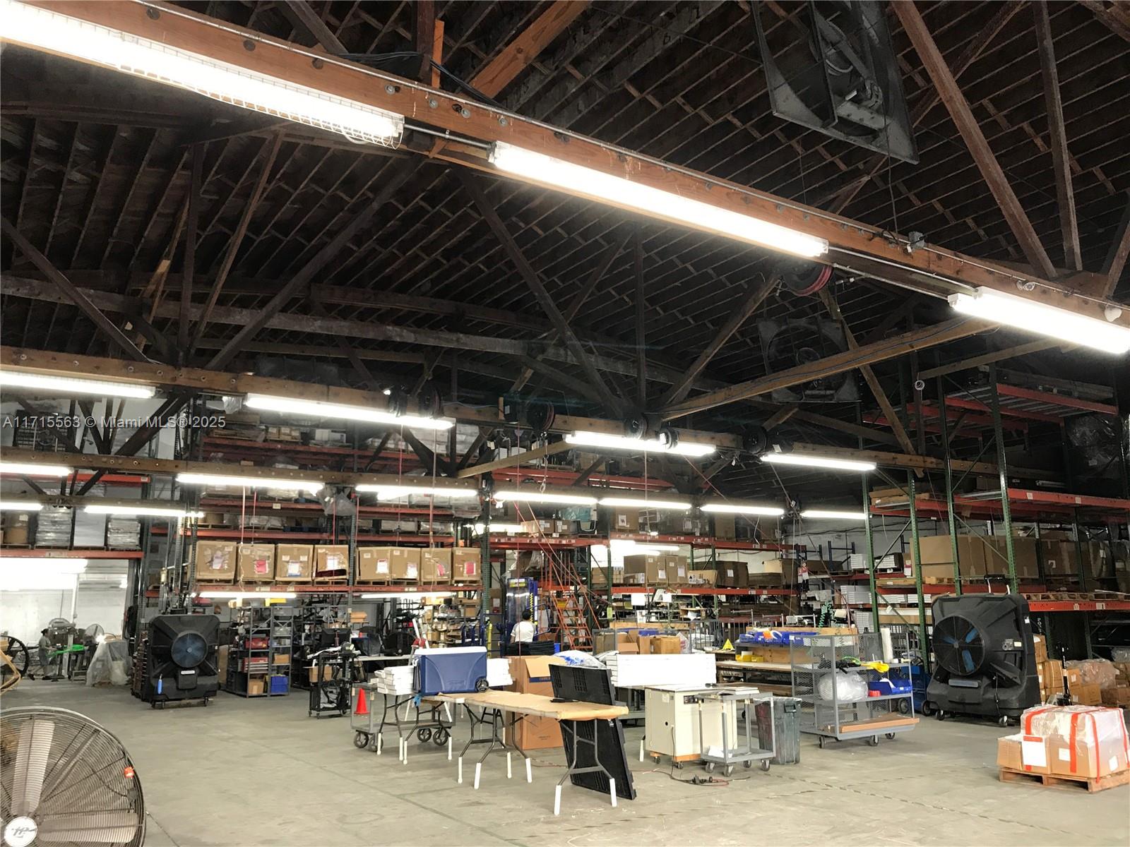 This industrial warehouse space features high exposed wooden rafters, overhead lighting, and metal storage shelving — 1628 NW 28th St, Miami FL 33142, MIAMI, FL