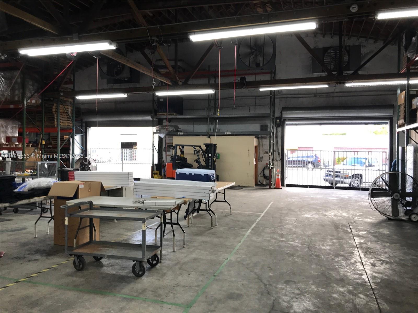 An industrial warehouse space features concrete floors, overhead lighting, and two large open bay doors — 1628 NW 28th St, Miami FL 33142, MIAMI, FL