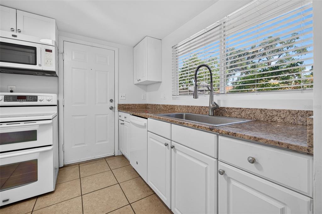 A kitchen features white cabinets, granite countertops, a white stove, and a window with blinds — 1162 HIGHLAND STREET N, ST PETERSBURG, FL