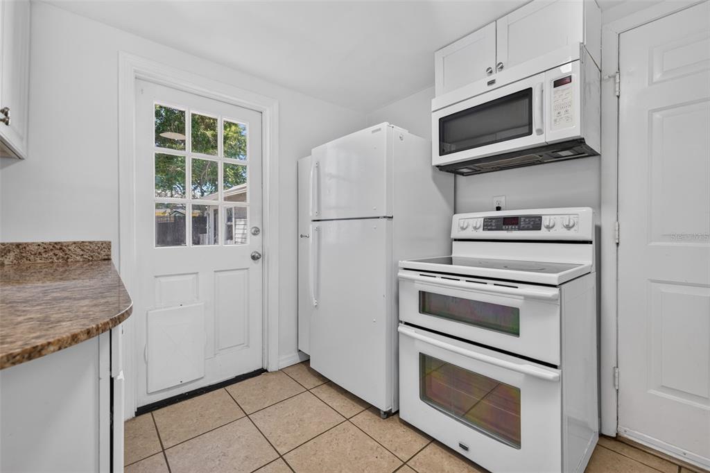 A kitchen with white appliances, granite countertops, tile flooring, and a glass-paneled exterior door — 1162 HIGHLAND STREET N, ST PETERSBURG, FL