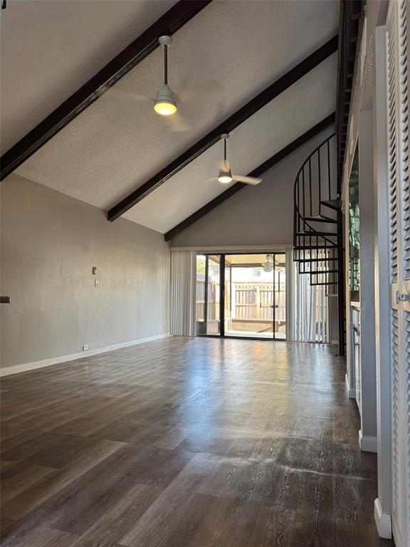 An empty living room features vaulted ceilings with exposed beams, wood-look flooring, and a spiral staircase — 4008 MURIEL PLACE UNIT 1, TAMPA, FL
