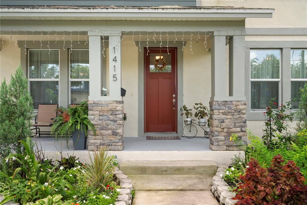 A front porch with a red door, stone-based columns, and a landscaped garden — 1415 CRYSTAL LAKE DRIVE, LAKELAND, FL