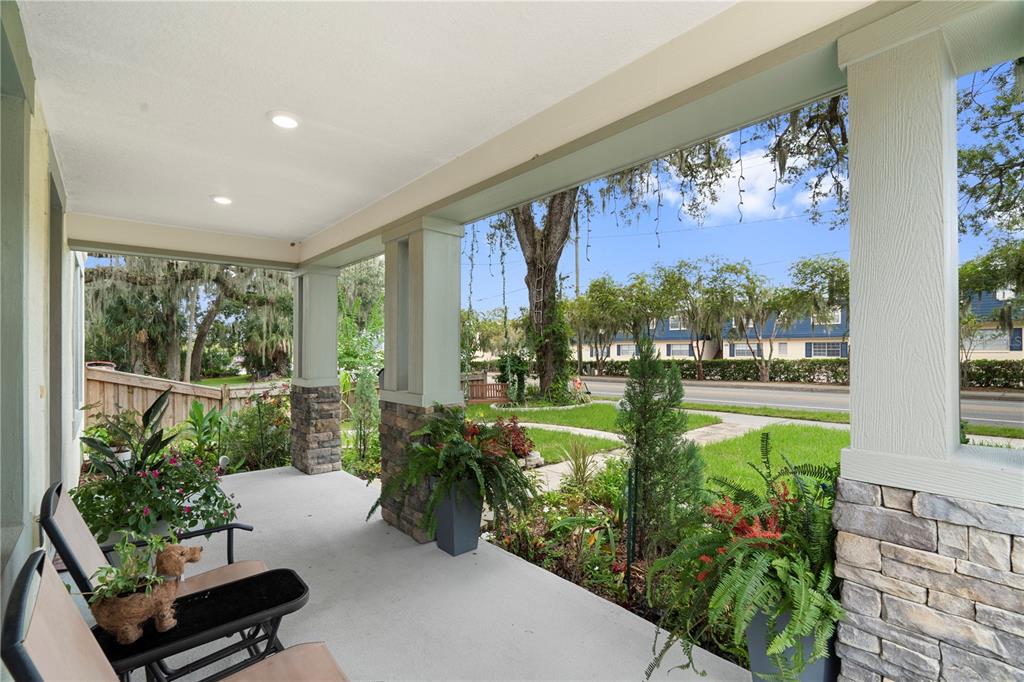 A covered front porch with stone pillars, potted plants, and two chairs overlooking a street — 1415 CRYSTAL LAKE DRIVE, LAKELAND, FL