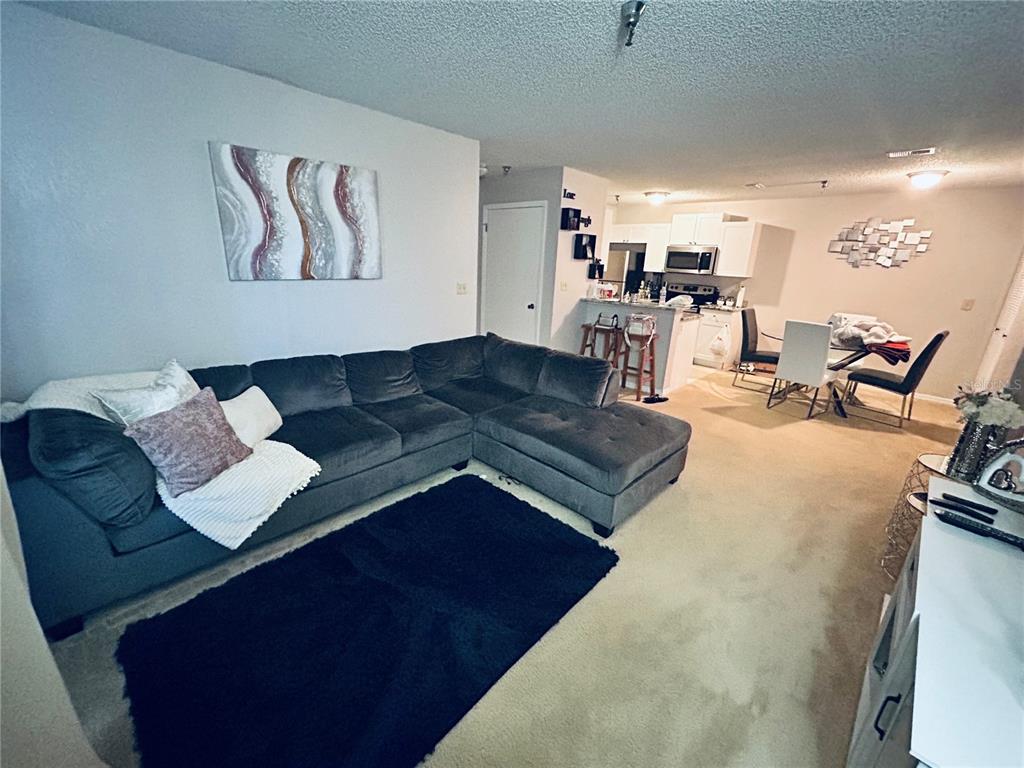 A living room with a gray sectional sofa, a dark rug, and an open kitchen — 10265 GANDY BOULEVARD N UNIT 1603, ST PETERSBURG, FL