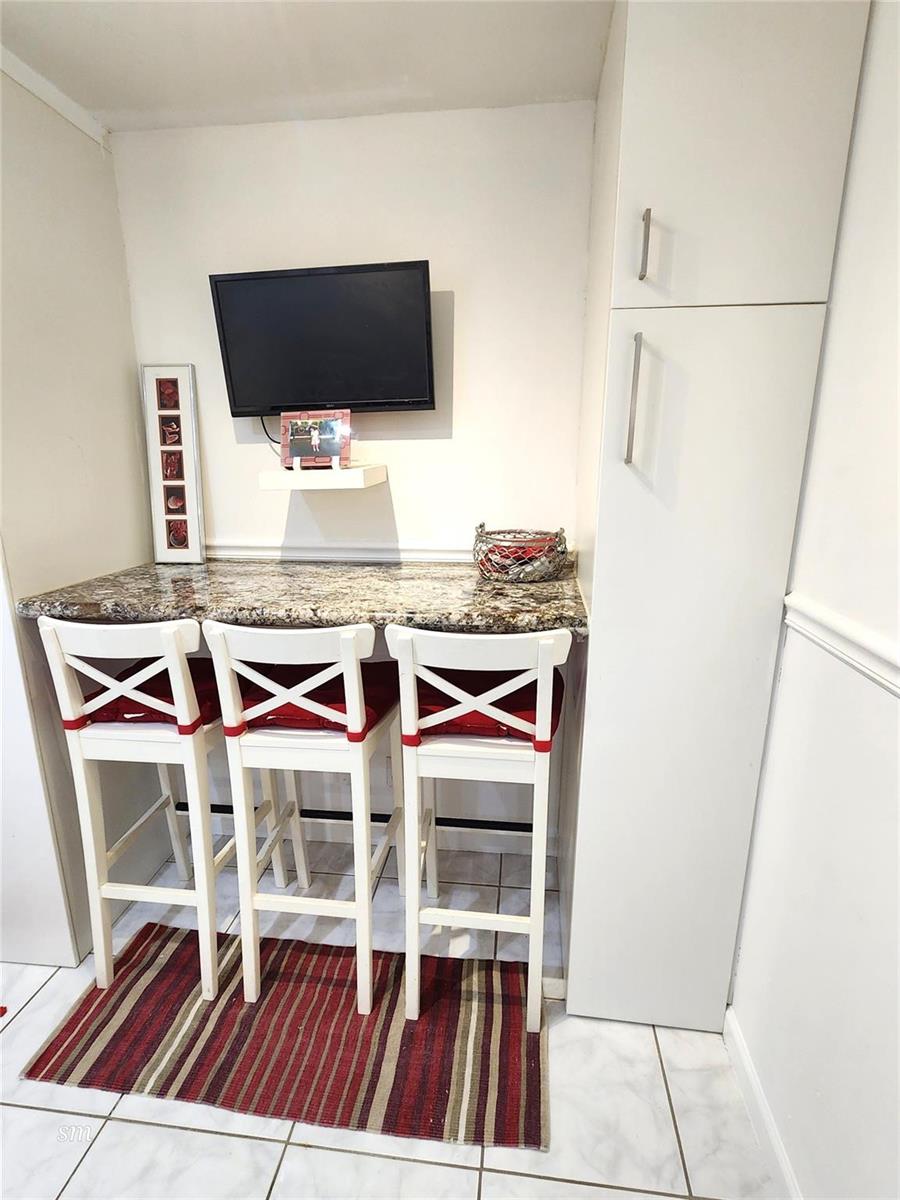 A breakfast bar with three white chairs sits beneath a wall-mounted television — 4400 Hillcrest Drive # 404, Hollywood FL 33021, HOLLYWOOD, FL