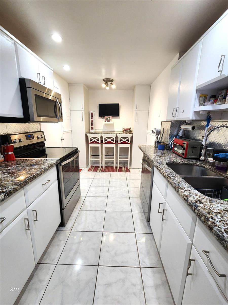 A galley kitchen features white cabinets, granite countertops, stainless steel appliances, and a breakfast bar — 4400 Hillcrest Drive # 404, Hollywood FL 33021, HOLLYWOOD, FL