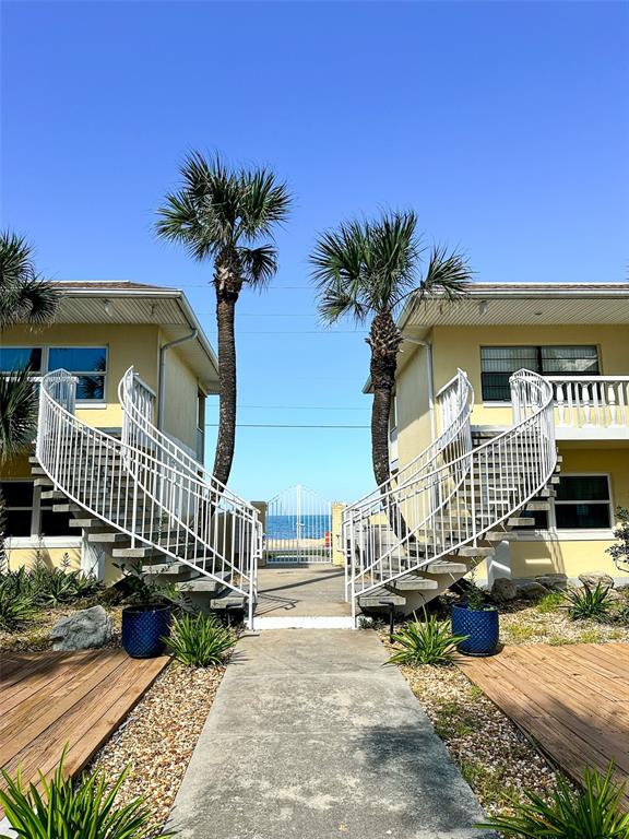 Two yellow buildings with curved white staircases face a central walkway leading to the beach — 2780 OCEAN SHORE BOULEVARD UNIT 8S, ORMOND BEACH, FL