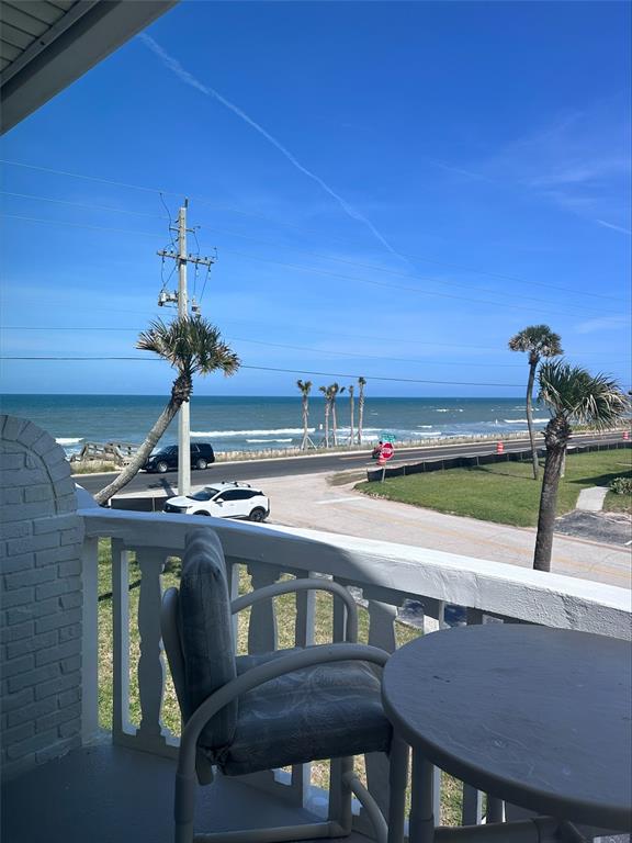 A balcony with a table and chair overlooks a coastal road, palm trees, and ocean — 2780 OCEAN SHORE BOULEVARD UNIT 8S, ORMOND BEACH, FL