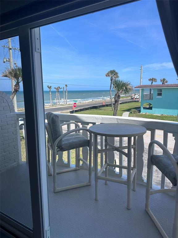 A balcony with a small table and two chairs overlooks a coastal road and ocean — 2780 OCEAN SHORE BOULEVARD UNIT 8S, ORMOND BEACH, FL