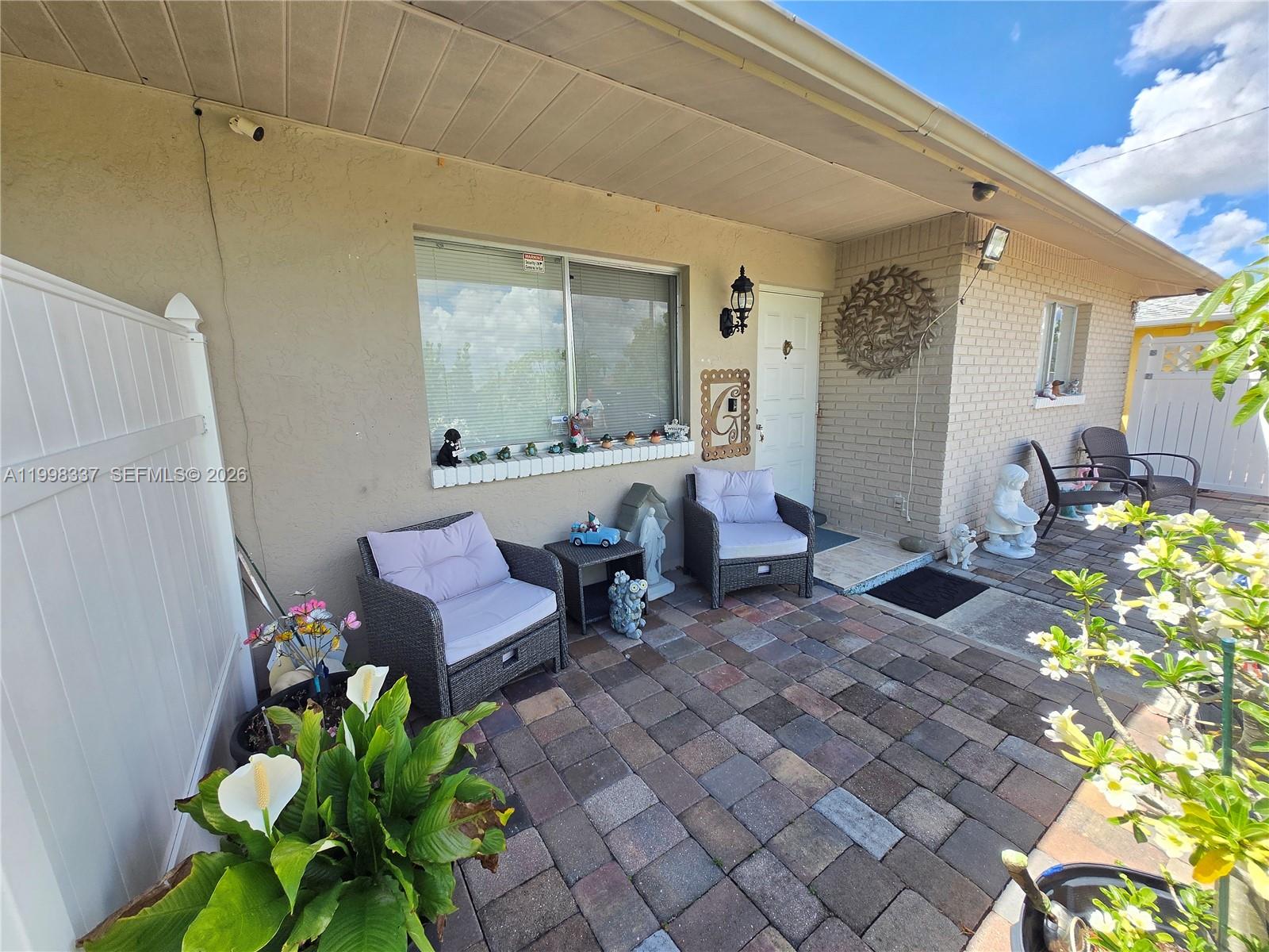 A paved patio features two wicker chairs, decorative figurines, and a brick exterior wall — 712 SE 8th St, Cape Coral FL 33990, CAPE CORAL, FL