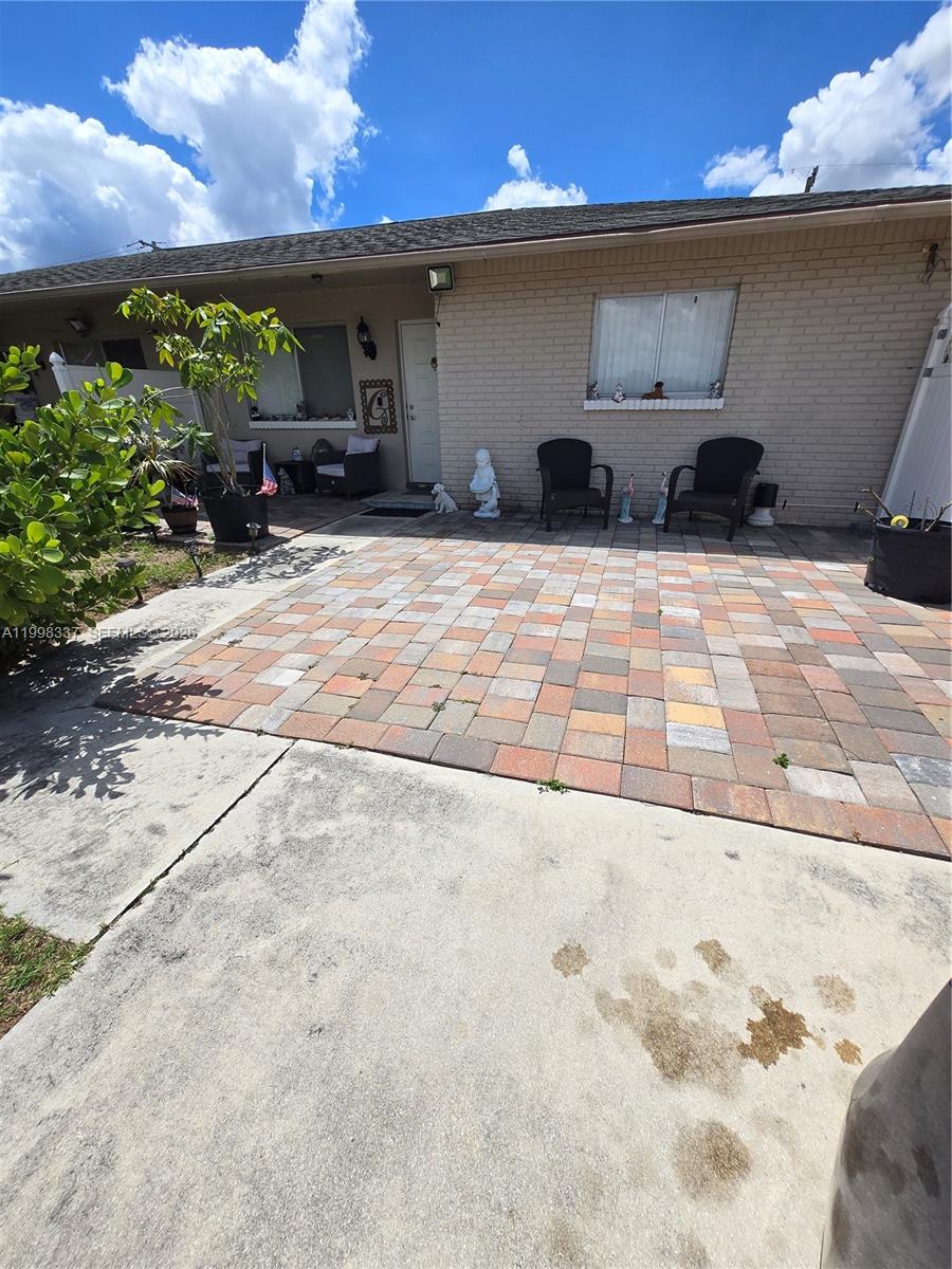 A brick house exterior features a paved patio area with two chairs and potted plants — 712 SE 8th St, Cape Coral FL 33990, CAPE CORAL, FL