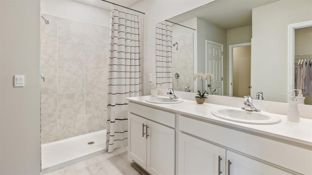 A bathroom with a double vanity, white cabinets, and a tiled shower with a curtain — 16435 BECASSE DRIVE, PUNTA GORDA, FL