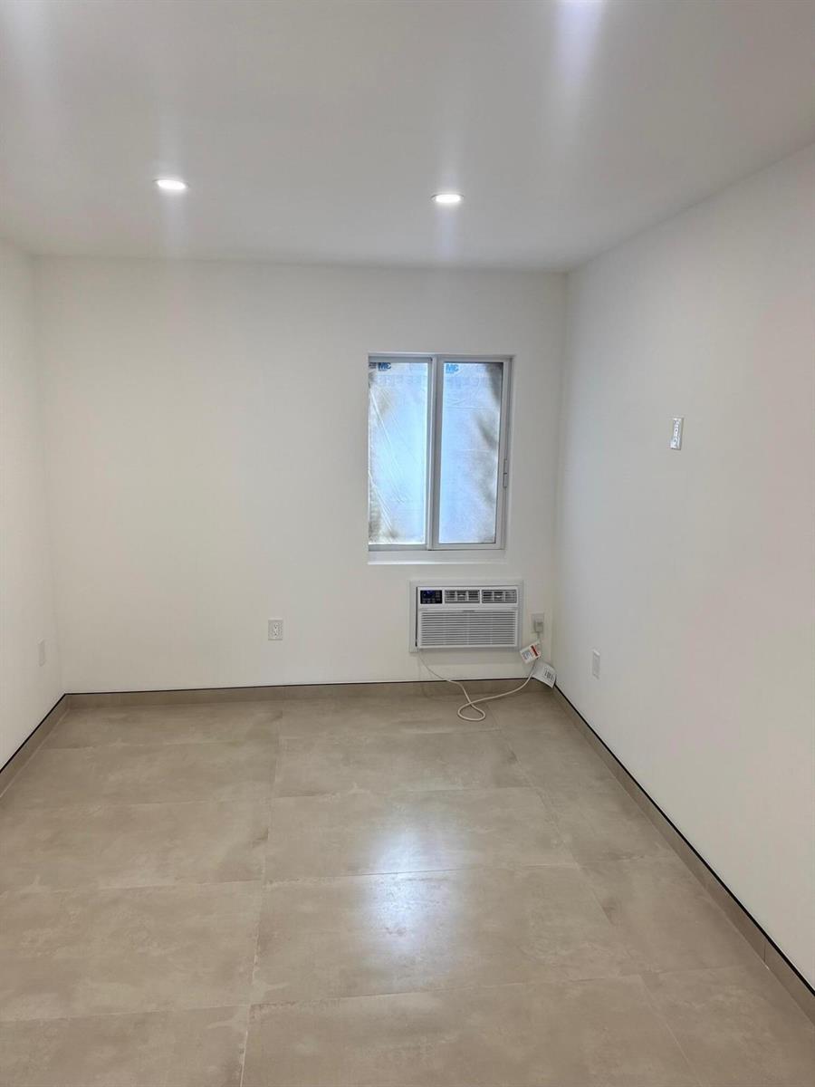 An empty room with white walls, light tile flooring, a window, and a wall-mounted air conditioner — 1235 Normandy Drive # 10, Miami Beach FL 33141, MIAMI BEACH, FL