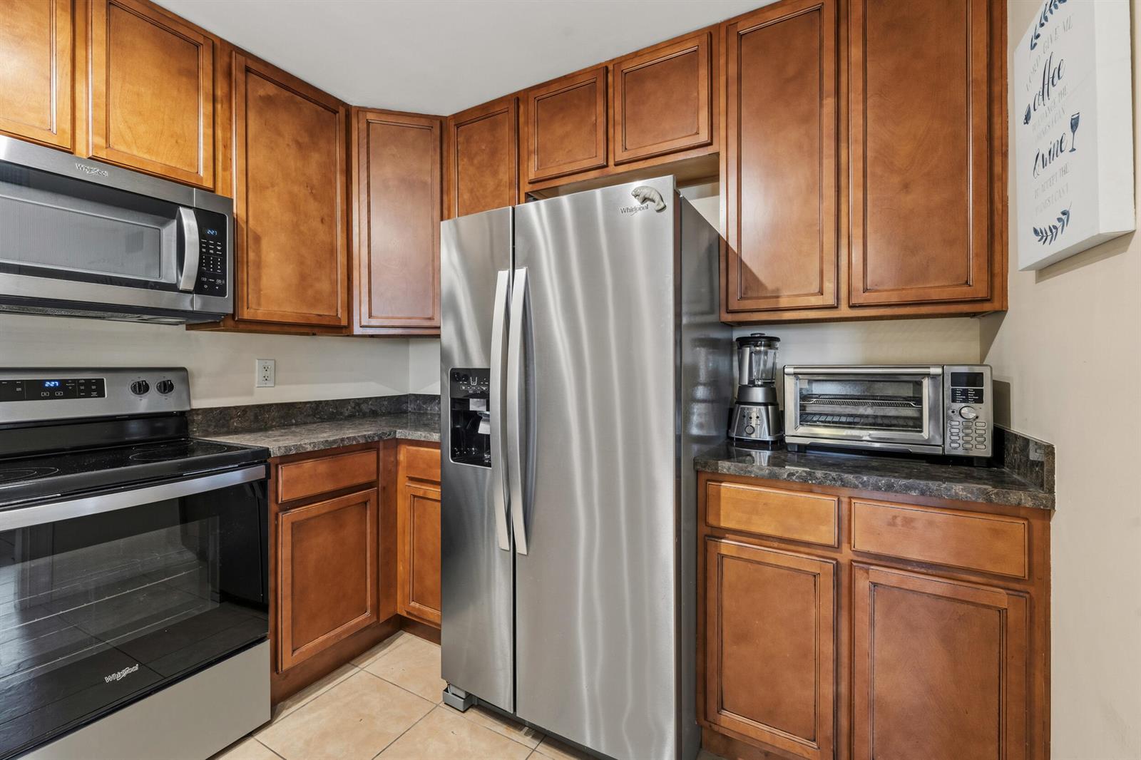 A kitchen features wood cabinets, stainless steel appliances, and dark countertops — 2050 Oleander Boulevard # 106, Fort Pierce FL 34950, FORT PIERCE, FL