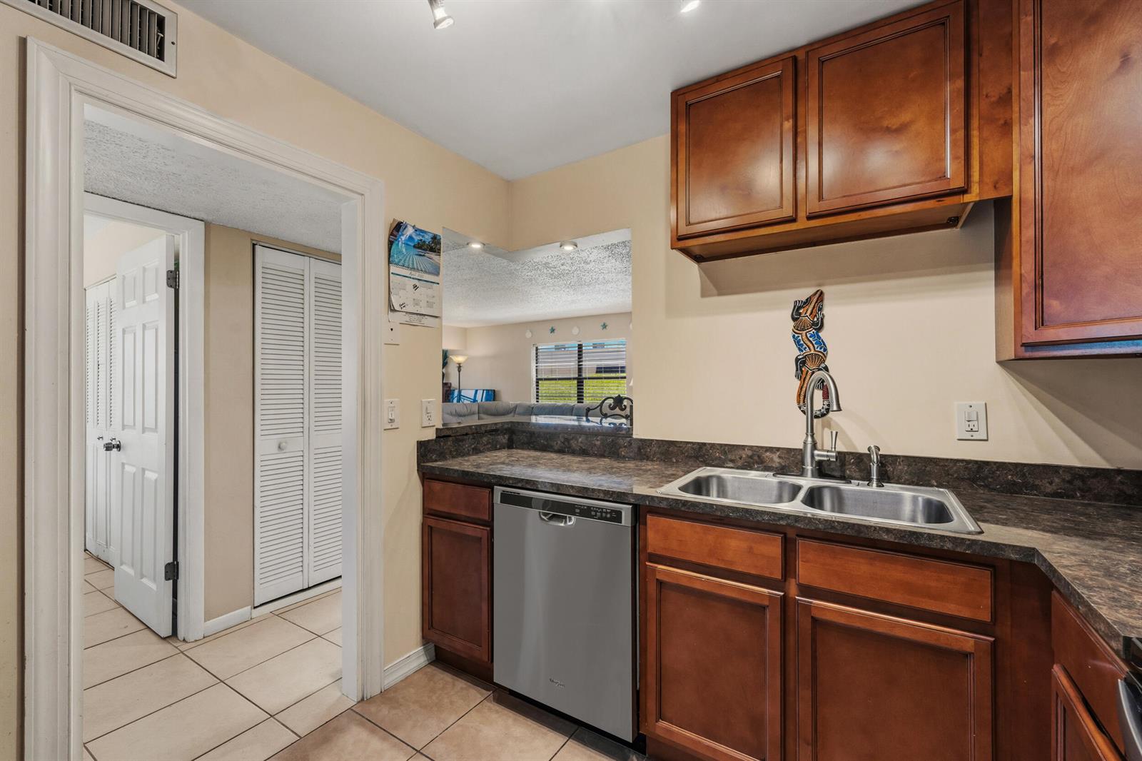 A kitchen featuring wood cabinets, dark laminate countertops, a stainless steel dishwasher, and a sink — 2050 Oleander Boulevard # 106, Fort Pierce FL 34950, FORT PIERCE, FL
