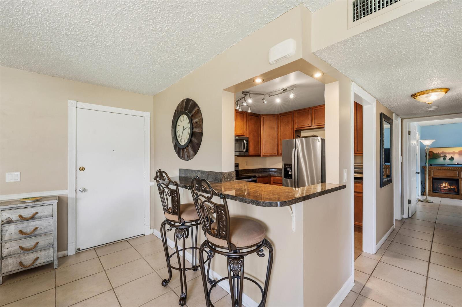 A kitchen with a breakfast bar, two stools, and a view into a living area — 2050 Oleander Boulevard # 106, Fort Pierce FL 34950, FORT PIERCE, FL
