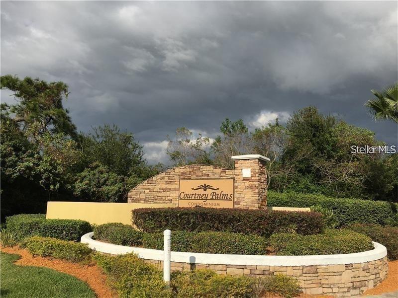 A stone monument sign for Courtney Palms Condominium stands in front of trees and clouds — 10019 COURTNEY PALMS BOULEVARD UNIT 303, TAMPA, FL