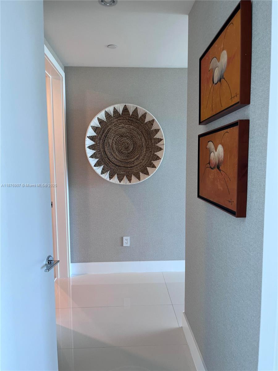 A hallway features white tile floors, gray textured walls, a woven wall hanging, and artwork — 10201 Collins Ave # 301, Bal Harbour FL 33154, BAL HARBOUR, FL